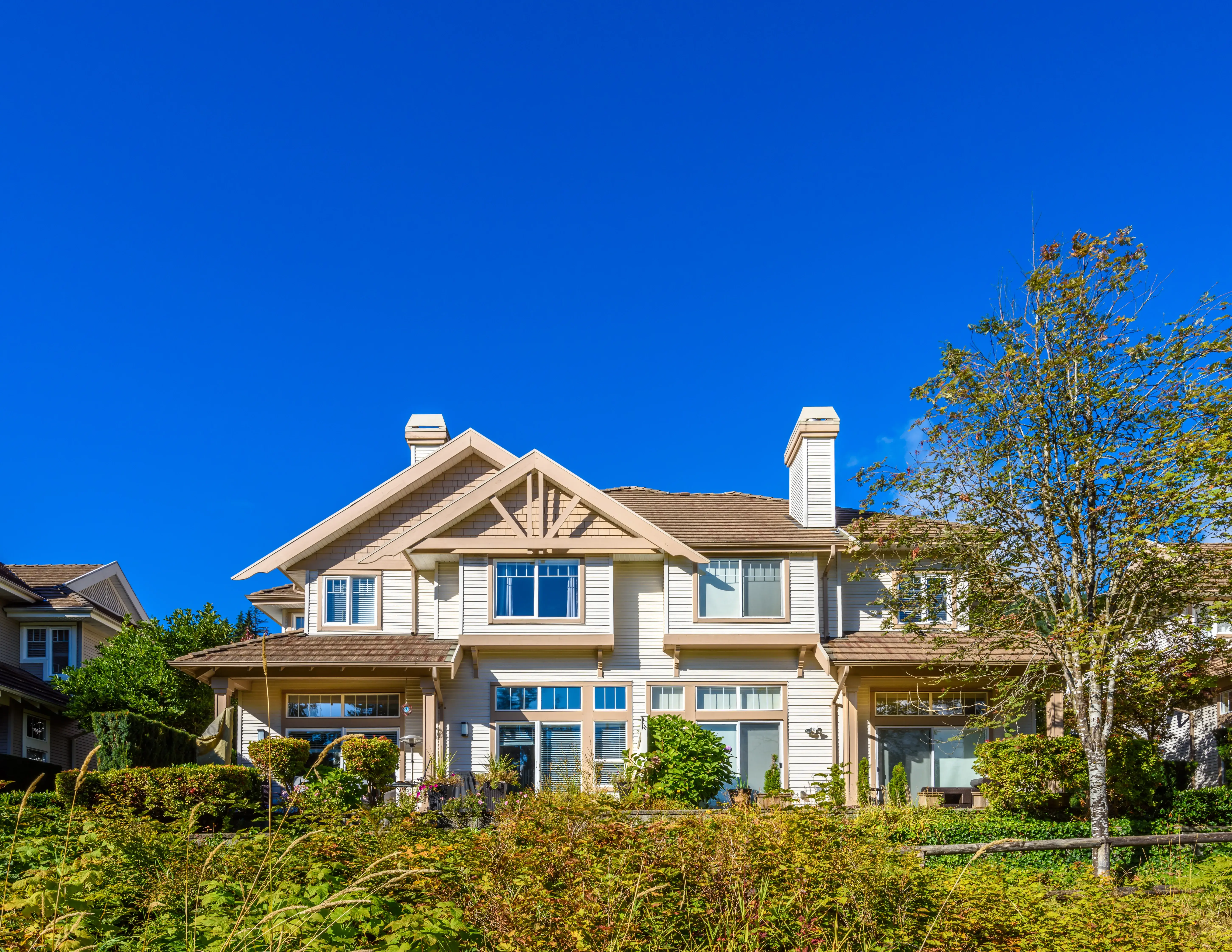 A large craftsman-style home with a lush garden on a clear summer day
