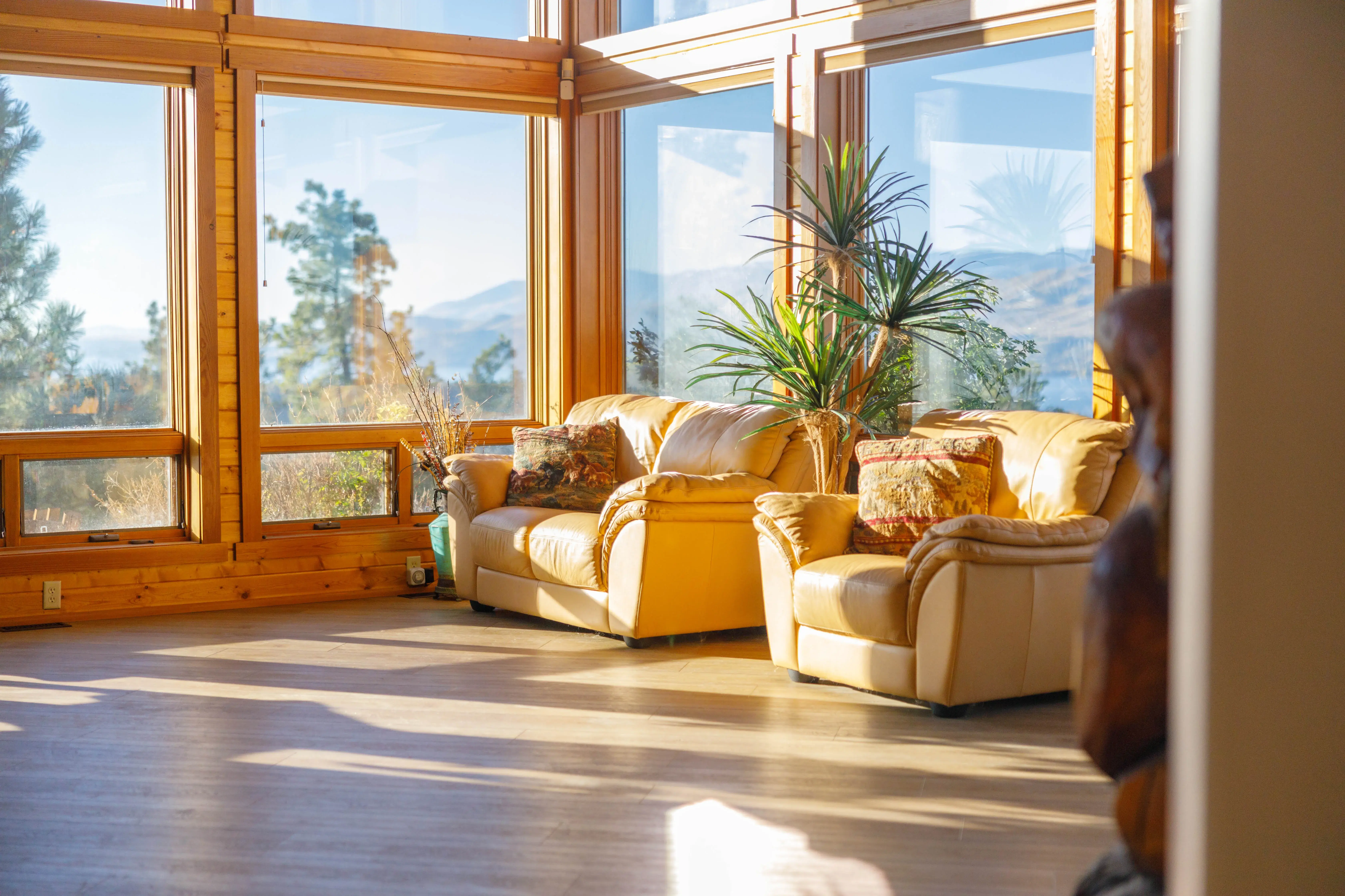 A sunlit living room with leather sofas and mountain views through tall windows